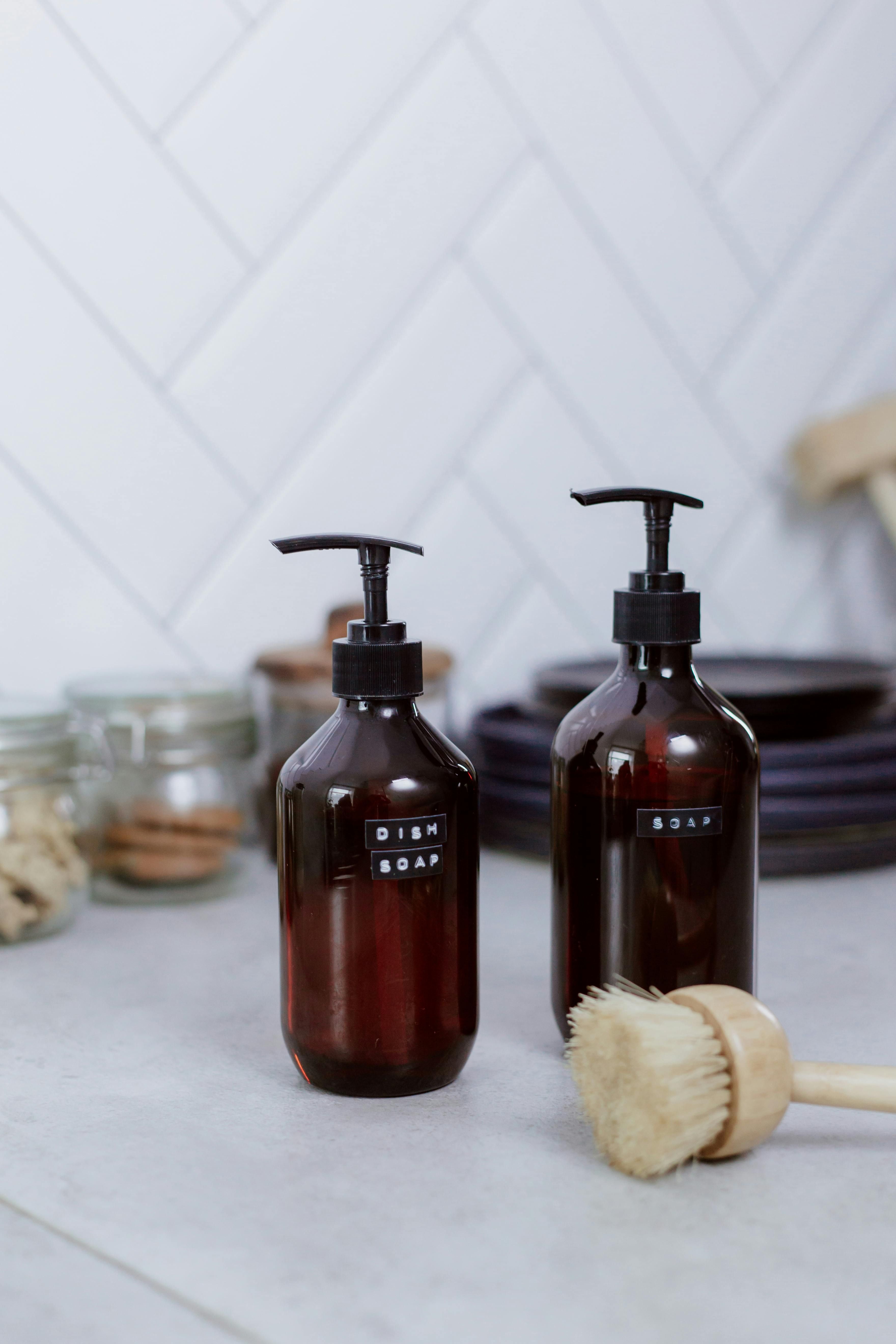 Two cleaning soap bottles and a scrub brush on a kitchen counter